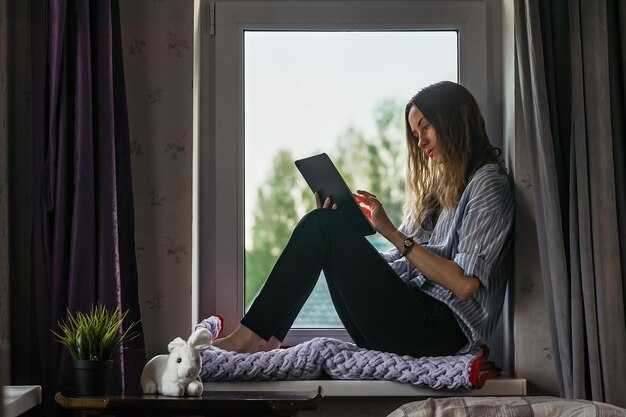 Studente communiceert en studeert thuis bij het raam op de tablet