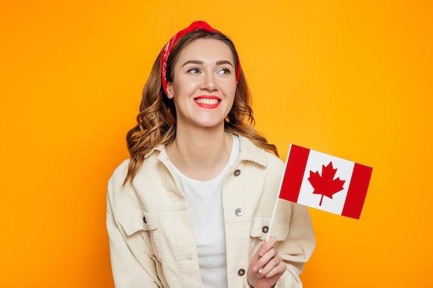 Studente die en een kleine vlag van Canada glimlacht houdt die over oranje achtergrond wordt geïsoleerd