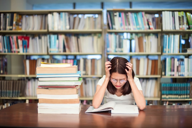 Studente met glazen die boeken in de bibliotheek lezen