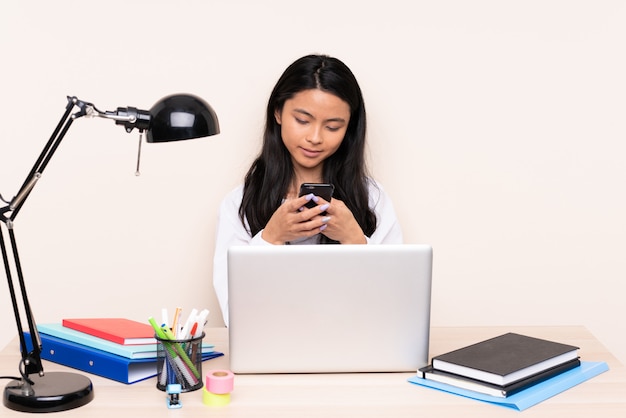 Studenten aziatisch meisje in een werkplaats met laptop die op beige wordt geïsoleerd