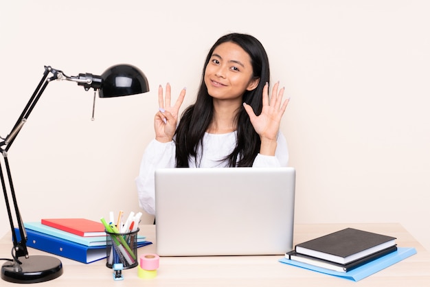 Studenten Aziatisch meisje in een werkplaats met laptop op beige muur die acht met vingers tellen