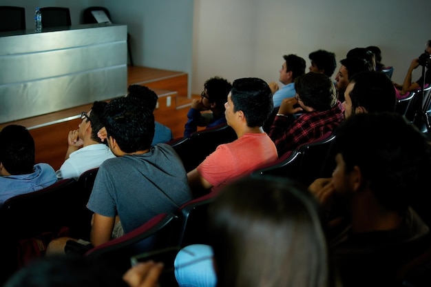 Studenten die aandacht besteden aan een lezing van een vrouw die projecteert over boeken en architectuuronderwijs