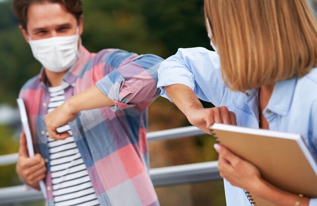 Foto studenten die maskers dragen tijdens het begroeten door ellebogen te gebruiken op de campus