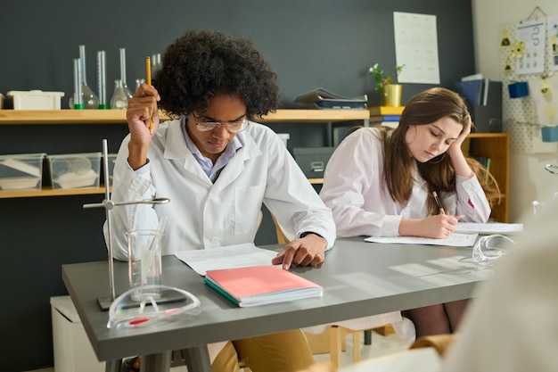 Foto studenten in laboratoriumjassen die individuele opdracht uitvoeren bij scheikundeles