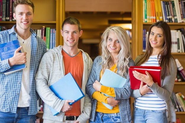 Studenten met mappen staande tegen boekenplank in de bibliotheek