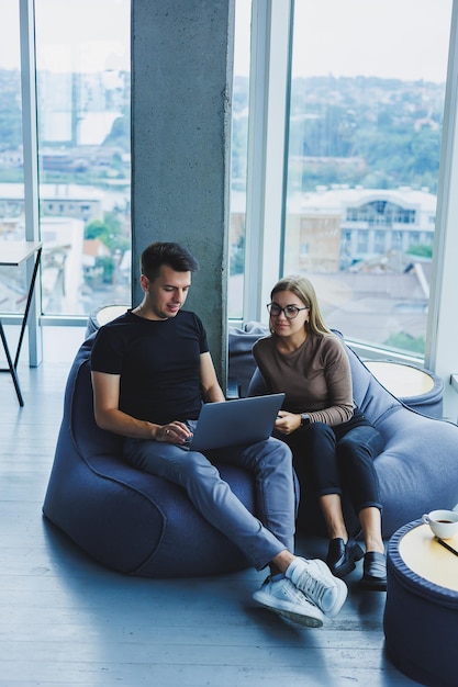 Studenten zitten in de werkruimte bij het raam en werken samen aan een project op een laptop Vrolijke collega's managers kijken samen naar de laptop en glimlachen