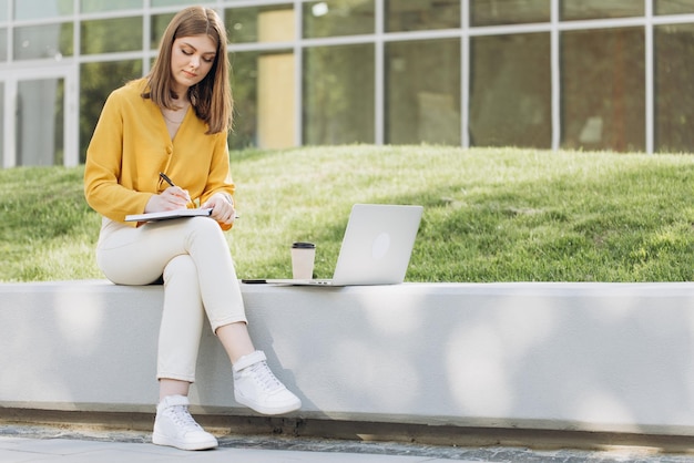 Studentenmeisje die les online bekijkt en buitenshuis studeert jonge vrouw die aantekeningen maakt terwijl ze kijkt