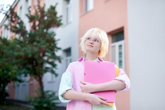 Studentenmeisje met roze map met boeken die bedachtzaam opkijken op de schoolcampus