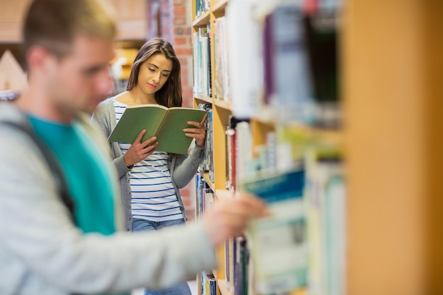 Студенты с книжной полкой в ​​библиотеке