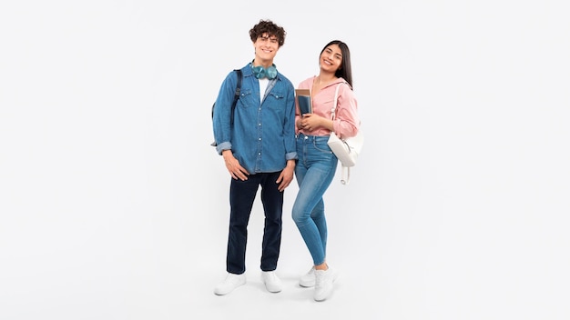 Students couple posing with workbooks and backpacks standing together studio