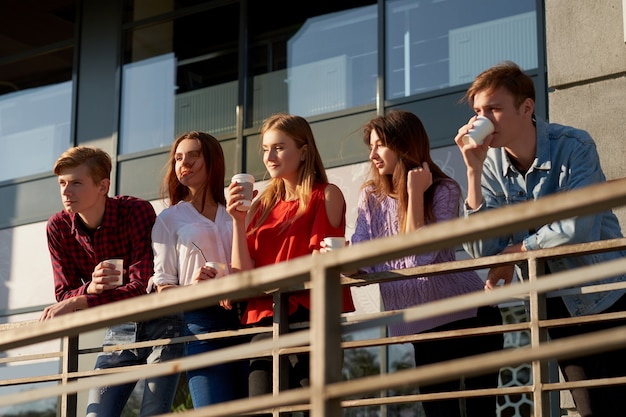 Students enjoying cup of coffee to go on street. Young people in the morning outdoor with cup of energy drink