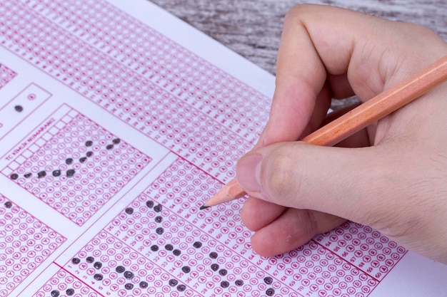 Students hand doing exams quiz test paper with pencil drawing selected choice on answer sheets at school