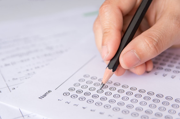 アンサーシートと数学の質問シートに選択した選択肢を書く鉛筆を持つ学生の手。試験をしている学生学校試験