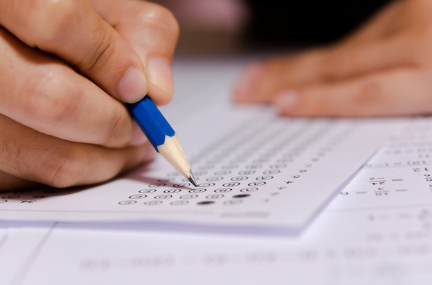 Photo students hand holding pencil writing selected choice on answer sheets