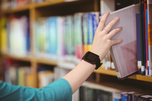 Students hand with smartwatch picking book from bookshelf