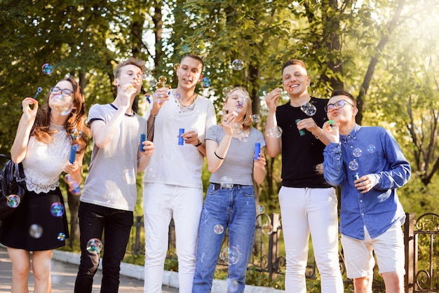 Students having fun, blowing soap bubbles in the park in the evening