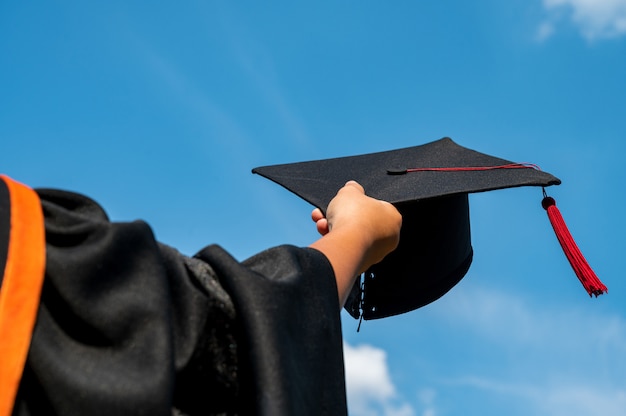明るい空の中で手で卒業帽のショットを保持している学生