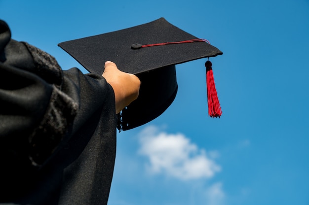 The students holding a shot of graduation cap by their hand in a bright sky