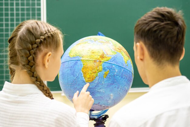 Фото Ученики в белых рубашках указывают место на глобусе урок географии вид сзади