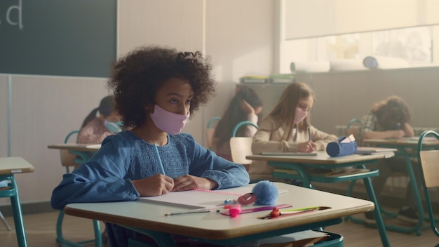 Students in medical masks sitting at school desks during coronavirus pandemic