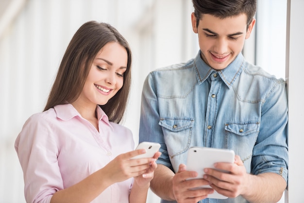 Students reading news on gadgets while standing at college.