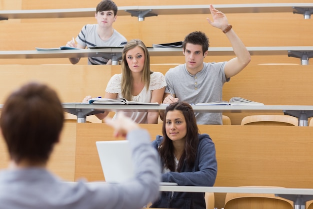 Students sitting at the lecture hall with man razing hand to ask question