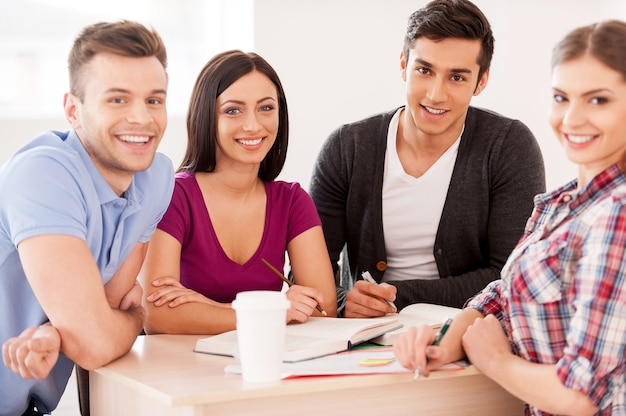 Students studying together. Four cheerful students studying sitting at the desk together and smiling at camera