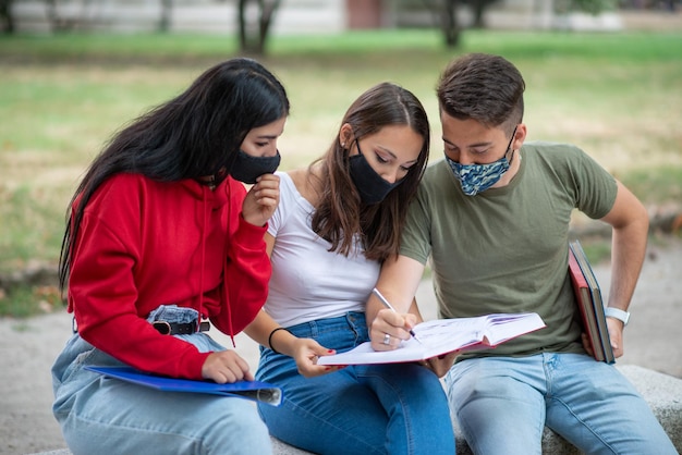 Students studying together sitting on a bench outdoor and wearing masks during coronavirus times