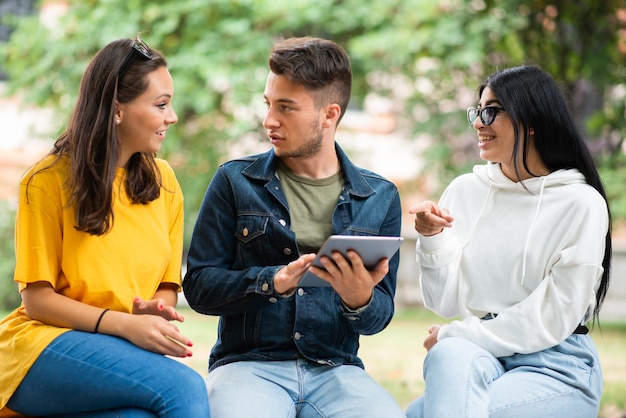 Students studying together with a digital tablet sitting on a bench outdoor