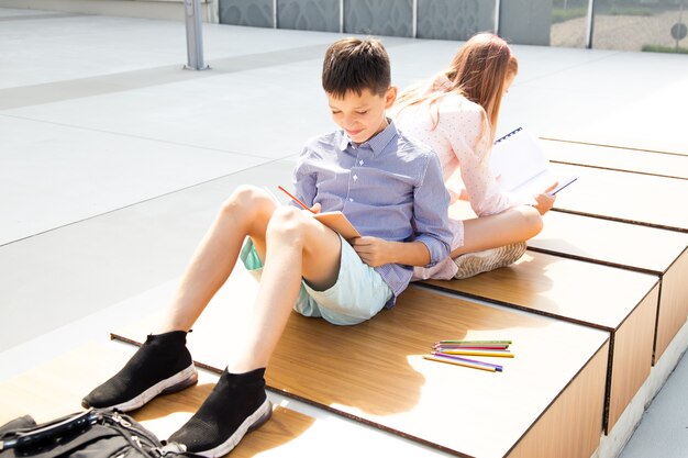 Students do their homework while sitting back-to-back in the schoolyard of campus. Friendship of teenagers