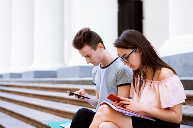 Students while break sitting on stairs of the university using mobile phones and paying no attention to one another