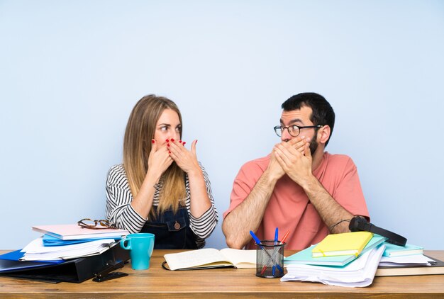 Studenti con molti libri che coprono la bocca con le mani