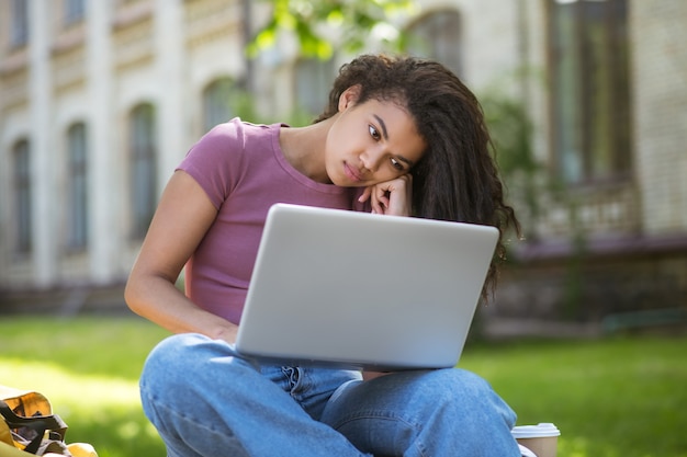 Foto studeren in het park. een meisje in een roze t-shirt met een laptop in het park