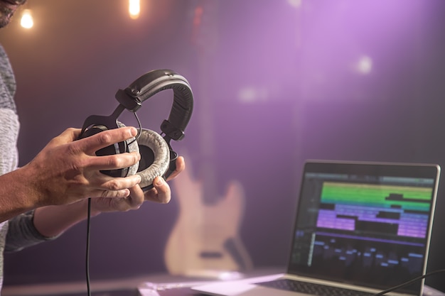 Студийные аудио наушники для записи звука в мужских руках на затуманенной стене студии музыкальной студии с монитором ноутбука крупным планом.