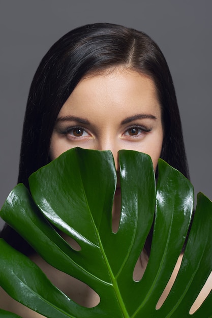 Studio bellezza ritratto di giovane bruna con pelle perfetta make-up naturale con foglia verde esotico