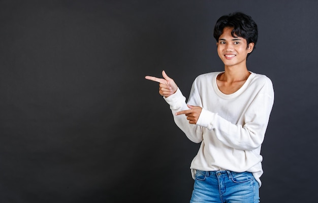 Studio close-up shot van Aziatische jonge Lgbtq gay glamour biseksueel homoseksueel mannelijk model in casual outfit staande glimlachend met twee handen en vingers wijzende lege kopie ruimte op zwarte achtergrond