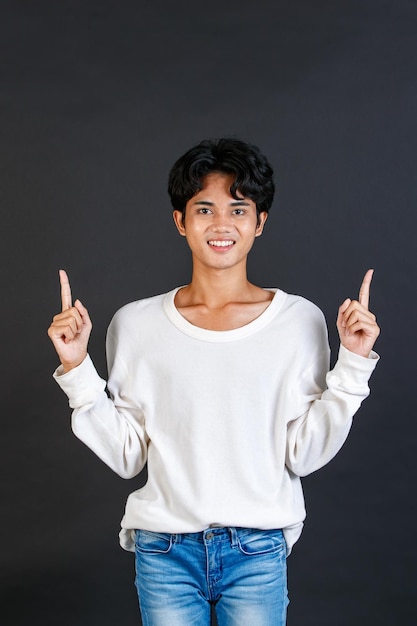 Studio closeup shot of Asian young LGBTQ gay glamour bisexual homosexual male model in casual outfit standing smiling holding two hands and fingers pointing blank copy space on black background