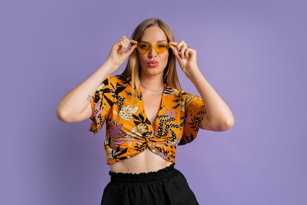 Studio fashion photo of pretty blond woman in stylish top and linen shorts posing on purple background