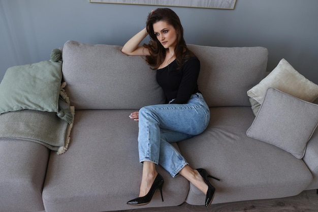Studio fashion shooting A young woman is sitting on the sofa in stylish shoes and jeans