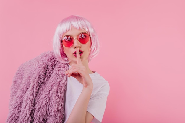 Studio foto van glamoureuze vrouwelijke model in zonnebril geïsoleerd op roze achtergrond Indoor portret van jocund jonge vrouw draagt stijlvolle peruke