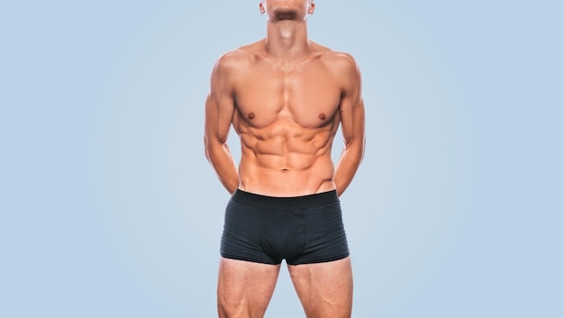 写真 青い背景に彼の腹部のプレスを示す黒い下着のフィットネス筋肉男性モデルのスタジオ画像セクシーな胴体を持つスポーティで健康的な強い運動スポーツマンのトリミングされた頭の肖像画