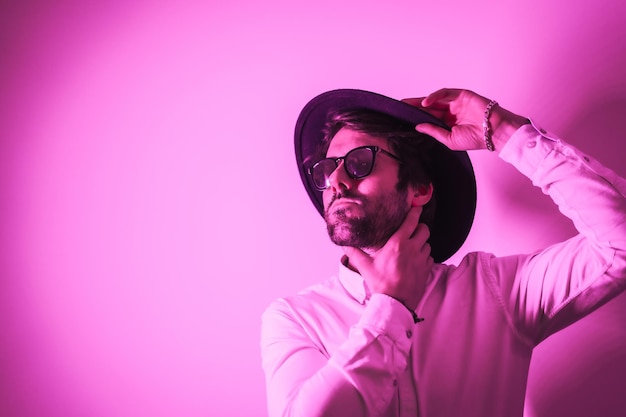 Studio lifestyle a young Caucasian man with a seductive look wearing sunglasses with neon pink light with copy and paste space