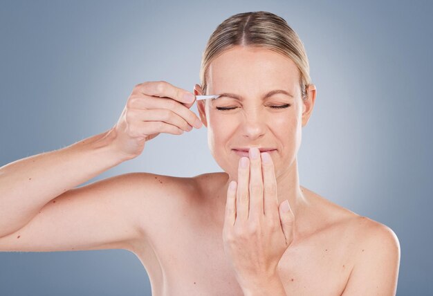 Foto studio-opname van een aantrekkelijke jonge vrouw die haar wenkbrauwen plukt tegen een grijze achtergrond