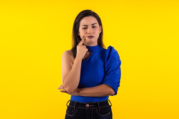 Studio-opname van een jonge vrouw in een bril met blauwe blouse op gele achtergrond met verschillende gezichtsuitdrukkingen