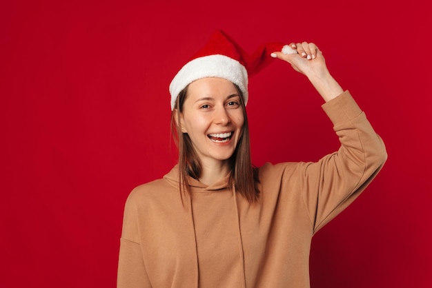 Foto studio-opname van een speelse vrouw met een kerstmuts die naar de camera lacht op rode achtergrond