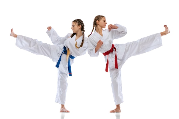 Studio-opname van twee tienermeisjes, taekwondo-atleten in uniforme training geïsoleerd op witte achtergrond
