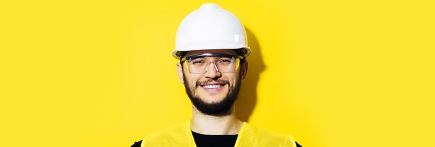 Studio panoramic portrait of young smiling construction engineer worker man, wearing safety helmet and goggles