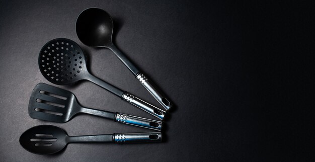 Studio photo of black plastic kitchen utensils, on the dark table.