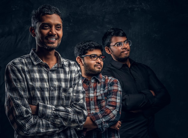 Студийное фото. Портрет трех индийских студентов в повседневной одежде на фоне темной текстурированной стены.