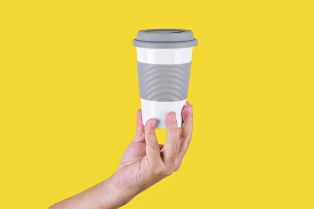 Studio photo with yellow background of a hand of a person holding recyclable take-away coffee cup